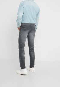 Camisa de mezclilla azul claro combinada con jeans ajustados de color gris. Los jeans tienen herrajes mínimos y bolsillos traseros, complementados con zapatillas blancas.