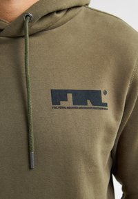 Hoodie verde oliva con un tessuto testurizzato, caratterizzato da un logo nero sul petto, cappuccio regolabile con lacci abbinati e dettagli in metallo.