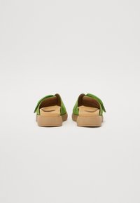 Žalios slip-on tipo bateliai su minkštu zomšiniu paviršiumi, apvalia nosimi ir rudos gumos padu. Nugaroje yra dekoratyvinis atvartas.