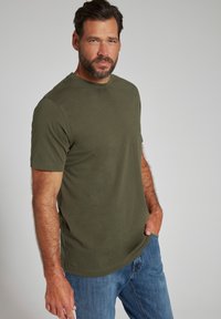 T-shirt in cotone verde oliva con maniche corte e colletto rotondo, abbinato a jeans in denim blu, esposto su uno sfondo neutro.