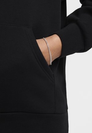 Svart hoodie i bomull med en frampocket där en hand syns delvis. Ett armband i silverkedja pryder handleden.