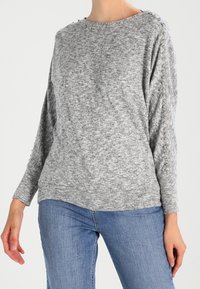 Harmaa neulepaita, jossa on pitkät hihat ja hopeiset niitit olkasaumoissa. Pehmeä kangas ja rento istuvuus.