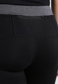 Czarne legginsy o dopasowanym kroju, z szarym elastycznym pasem, gładką fakturą i wzmocnionymi szwami.