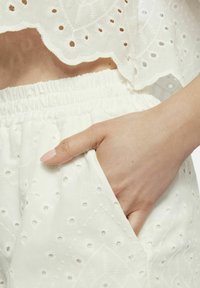 Wit geborduurd crop top met gegolfde randen, gecombineerd met witte shorts met een textuurpatroon en zijzak.