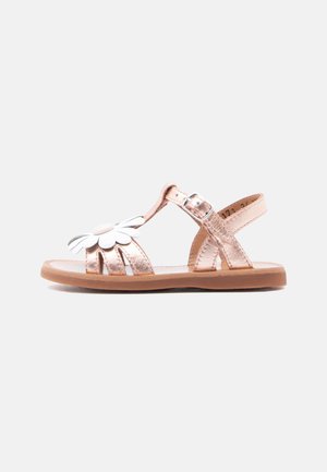 Metallic rosegold sandal i tumlingestørrelse med justerbar spænde og hvid blomstdekoration på den forreste rem, flad brun sål.