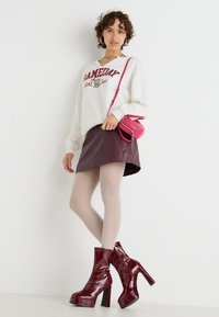 Hvit hettegenser med "GAMEDAY" trykk, bordeaux faux skinn skjørt, gjennomsiktige tights, og skinnende burgunder ankelstøvler med høye blokkhæler. Rosa crossbody veske.