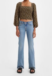 Top corto negro con estampado floral y mangas abullonadas, escote cuadrado. Vaqueros acampanados de color azul claro con un diseño clásico de cinco bolsillos. Sandalias de slide negras.