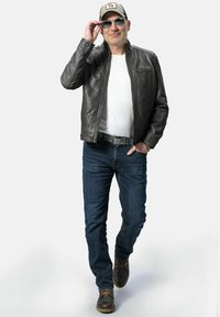 Leren jack in donkergrijs, wit T-shirt, blauwe spijkerbroek, bruine laarzen. Accessoires zijn een zonnebril en een grijze honkbalpet.