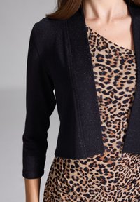 Schwarze cropped Strickjacke mit schimmernder Textur, kombiniert mit einem Leopardendruckkleid, das eine figurbetonte Silhouette und einen drapierten Stoff aufweist.