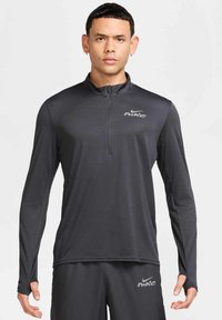 Nike Herren-Langarmshirt in Dunkelgrau aus glattem Stoff, mit einem Viertel-Reißverschluss, Daumenlöchern und reflektierendem Logo auf der Brust.