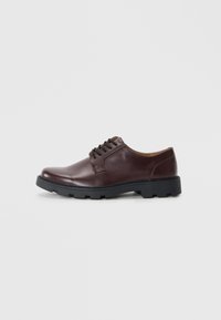 Zapato de piel marrón con cordones, punta redondeada, suela de goma negra y detalles en marrón contrastante en la lengüeta y el forro.