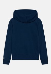 Marinblå hoodie, mjukt material, långa ärmar, ribbade muddar och nederkant, med logotypdetalj på vänster ärm.