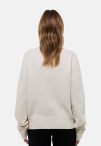 Pull ample beige clair avec ourlets et poignets côtelés, texture douce et design à épaule tombante, vu de dos.