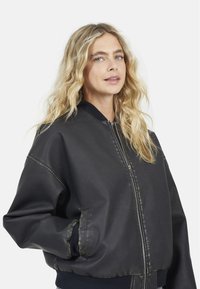 Giubbotto bomber in pelle nera con zip frontale, polsini e vita a coste. Presenta una texture liscia e dettagli di cucitura sottili.