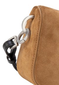 Braune Wildledertaschenecke mit schwarzem Lederband, befestigt durch zwei silberne Metallringe und eine silberne quadratische Schnalle.