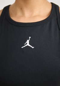 Črn rebrast top brez rokavov z belim embosiranim logotipom Air Jordan na prednjem delu. Ovratnik je okrogel, tkanina pa se zdi mehka.