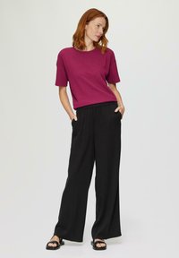 Magenta getextureerde gebreide top met korte mouwen, gecombineerd met zwarte wijde broek. De outfit heeft een relaxte pasvorm met zijzakken en platte sandalen.