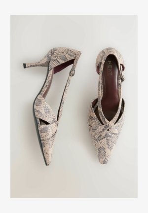 Zapatos de tacón con punta puntiaguda, hechos de material texturizado beige con un patrón de piel de serpiente. Incluyen ribete negro y detalle de correa en el tobillo.