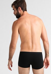 Zwarte boxershorts met een soepele textuur en een elastische tailleband. Geplaatst op een mannelijke model, waarbij het achteraanzicht wordt getoond. Minimalistisch ontwerp.
