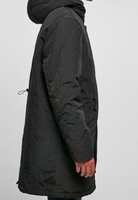 Černá vycpaná bunda s kapucí, s uzávěrem na zip a nastavitelnými šňůrkami, texturovaná tkanina a boční kapsy.