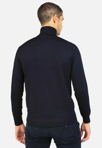Maglione a collo alto blu navy, texture a costine, design aderente, maniche lunghe e orlo a costine. Indossato vista da dietro, senza dettagli visibili.