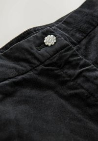 Melnas auduma bikses ar gludu tekstūru, ietverot dekoratīvu sudrabaini zieda formas pogu, dekorētu ar caurspīdīgām rhinestones.