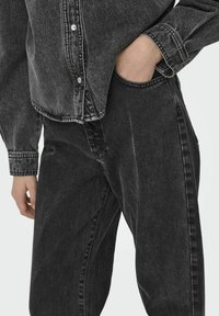 Camisa de mezclilla negra con cierre de botones y mangas largas, combinada con pantalones de mezclilla negra a juego, ambos con un acabado texturizado.