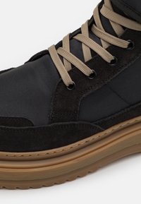 Bota de ante negro y nylon con cordones beige, plantilla acolchada y suela de goma texturizada. Presenta ojales y acentos cosidos.