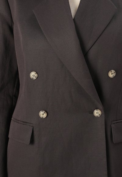 Blazer doppiopetto marrone scuro con revers marcati, due tasche frontali e bottoni argentati per la chiusura. Tessuto strutturato visibile.