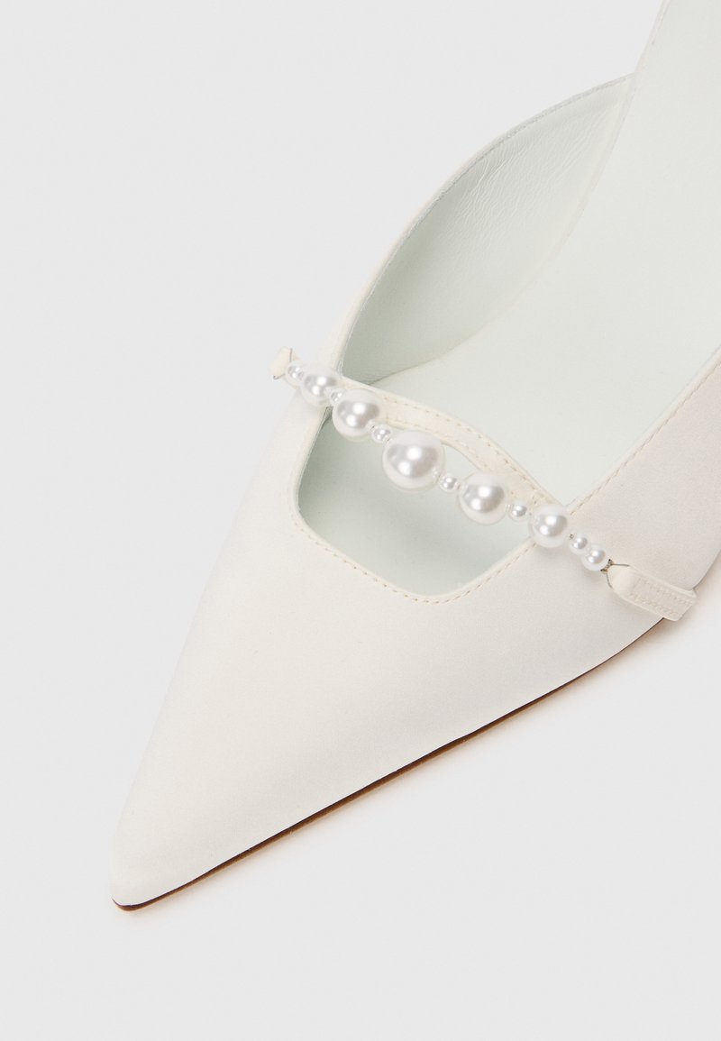 Décolleté in satin bianco con punta affilata e design a taglio, caratterizzato da una cinturini decorato con perline finte grandi e piccole alternatamente. Texture liscia.