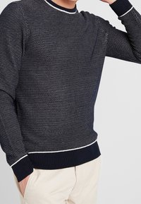 Maglione lavorato a maglia blu navy con un motivo testurizzato, dettagli bianchi al colletto e all'orlo, e polsini a coste. Adatto per un look casual.
