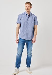 Kurzärmliges, hellblaues Hemd mit Knöpfen und einer Brusttasche. Getragen mit hellblauen Jeans und weißen Sneakers. Glatte Stofftextur.