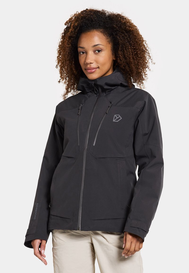 Veste noire imperméable avec un col haut, fermeture éclair à l'avant, deux poches sur la poitrine et capuche ajustable. Tissu texturé avec détail du logo sur la manche.