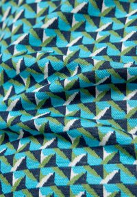 Baumwollstoff mit einem geometrischen Muster aus Dreiecken in Blau-, Grün- und Weißtönen auf blauem Hintergrund. Strukturierte Webart.