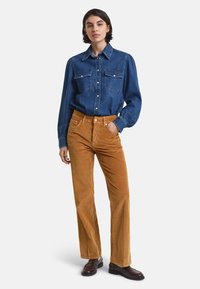 Blauwe denim shirt met twee borstzakken, gecombineerd met bruine corduroy broek, rechte pasvorm, gedragen met bruine leren schoenen.