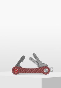 Röd mönstrad multifunktionstool med ett strukturerat handtag, som innehåller olika metallverktyg, inklusive en kniv och nyckelhållare, på en vit yta.