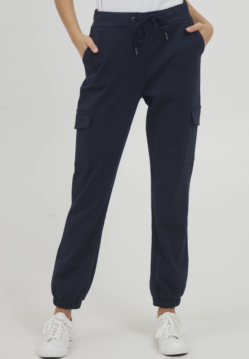 Marineblauwe joggerbroek met elastische tailleband, koordsluiting en zijzakken. Voorzien van ribgebreide enkelmanchetten en cargostijl zijzakken.