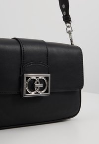 Black leather handbag with silver double-ring clasp and detachable strap, shown against plain light background.