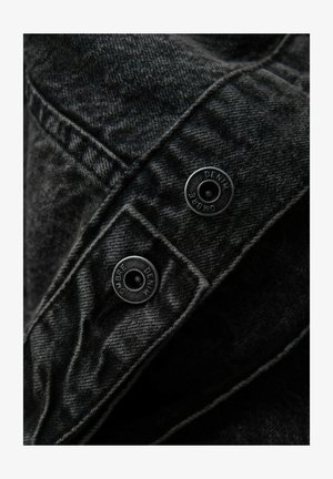 Musta farkkukangas, jossa on tekstuuripinta, varustettuna kahdella kaiverretulla metallinapilla, joissa lukee "DENIM", sulkemista varten kerrosrakenteessa.