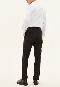 Camicia bianca a maniche lunghe e pantaloni neri eleganti indossati insieme. La camicia presenta un colletto classico; i pantaloni hanno una vestibilità sartoriale e tasche laterali.
