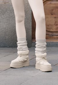 Beżowe buty na platformie z miękką tekstylną cholewką, luźnymi dzianinowymi mankietami i regulowanym sznurkiem. Gładka, jednolita podeszwa.