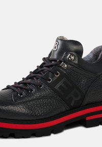 Czarny but z fakturowanej skóry, z czerwonymi akcentami, czarnymi sznurowadłami, wyściełanym kołnierzem i wyraźnym logo na boku.
