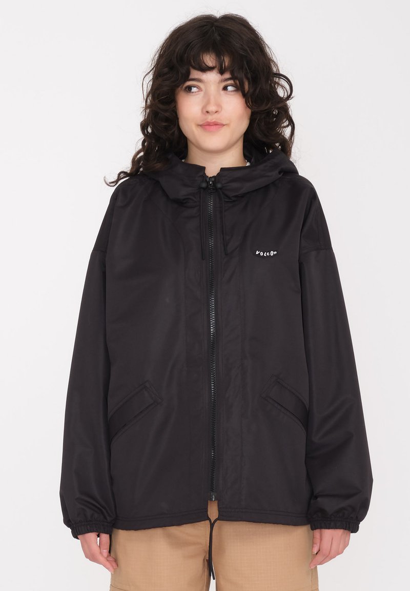 Veste noire imperméable avec capuche, fermeture éclair, deux poches latérales, poignets élastiques et ourlet à cordon; présente un logo sur la poitrine.