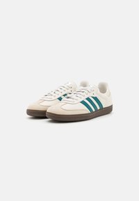 White and teal athletic shoes with three teal stripes, a textured brown rubber sole, and traditional lace-up design.
