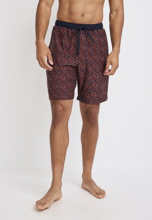 Herren-Schwimmshorts in Rot und Marineblau mit Chevron-Muster. Elastischer Bund mit Kordelzug, knielang, aus leichtem Material.