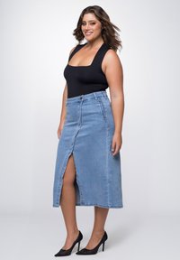 Blauwe denim rok met een voorknutsing en knoopsluiting, gecombineerd met een zwarte bodysuit. De outfit wordt aangevuld met zwarte hoge hakken.