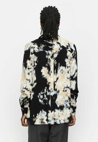 Langermig shirt van zwarte stof met een abstract crème en blauwe patroon, met een relaxte pasvorm en knoopsluiting.