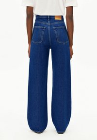 Weit geschnittene blaue Jeans aus Denim mit hoher Taille, zwei Gesäßtaschen und einem braunen Etikett auf der Rückseite. Vorderseitige Nähte sichtbar.