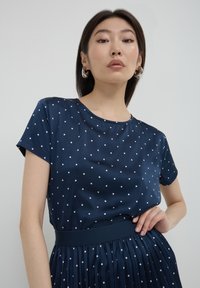 Abito blu navy con pois bianchi, maniche corte, scollo rotondo, vita elastica e gonna plissettata. Tessuto morbido.