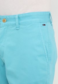 Světle modré bavlněné šortky s zipem, předními kapsami a dřevěným knoflíkem. Malé logo v červené, bílé a modré na pasu.